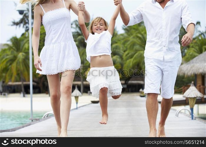 Parents Swinging Daughter As They Walk Along Wooden Jetty