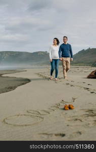 Parents taking a walk with baby name Oliver written in the sand next to his shoes. Selective focus on couple in background. Parents walking with baby name Oliver written in the sand