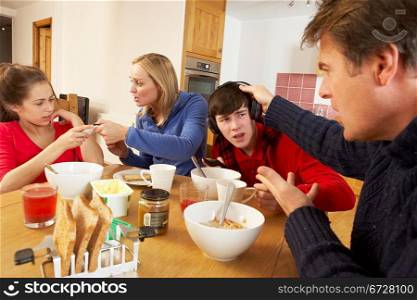 Parents Taking Away Gadgets From Children Whilst Eating Breakfast Together In Kitchen
