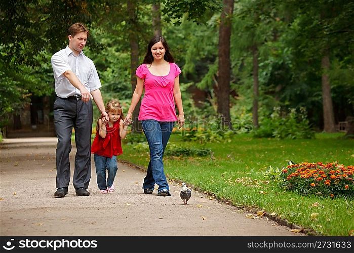 Parents together with daughter walk on summer garden. Man shows to girl of pigeon.