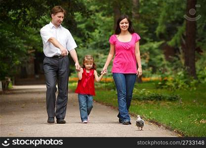 Parents together with daughter walk on summer garden. Man shows to girl of pigeon.