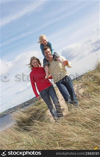 Parents walking with girl (5-6) on father&acute;s shoulders on dunes portrait