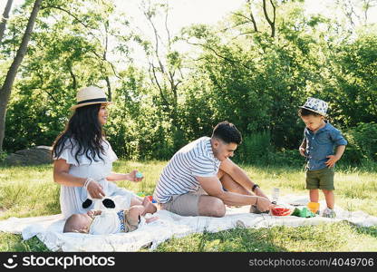 Parents with baby and toddler sons on picnic blanket in Pelham Bay Park, Bronx, New York, USA