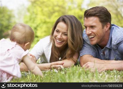 Parents With Baby Girl Sitting In Field Of Summer Flowers