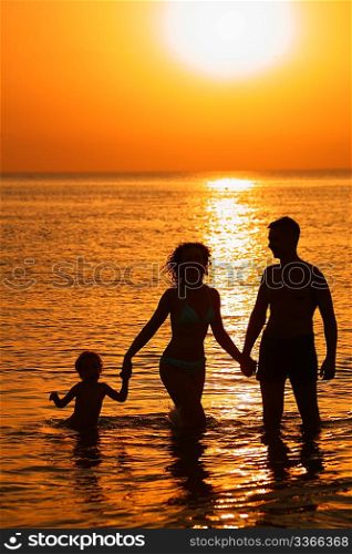Parents with child in sea on sunset