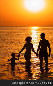 Parents with child in sea on sunset