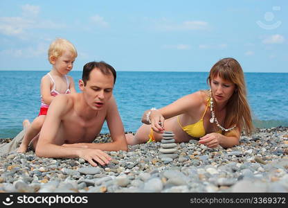 Parents with child on sea coast build pyramid of stones