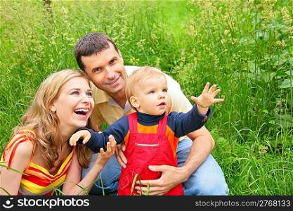 Parents with child sit in grass and look upwards