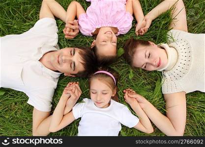 Parents with children lying on grass, view from top, head to head, having joined hands