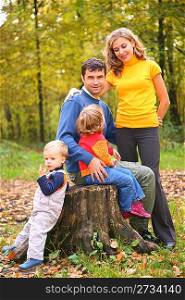 Parents with children sit on stub in forest in autumn