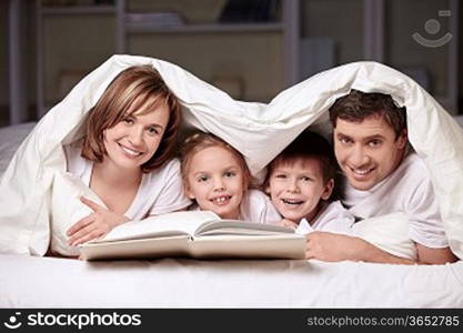 Parents with children under the blanket with a book