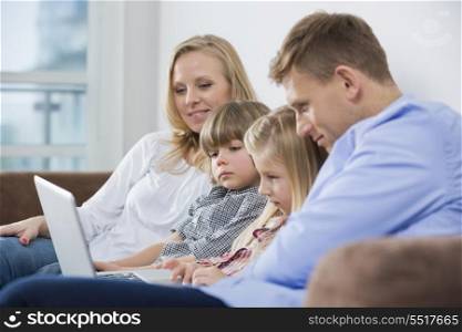 Parents with children using laptop on sofa at home