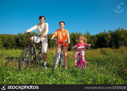 Parents with the daughter on bicycles in park a sunny day. Keep for hands.