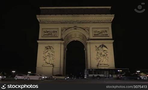 PARIS, FRANCE - SEPTEMBER 06, 2015: Low angle shot of car driving by Arc de Triomphe at night. Built in 19th century 50 metres monument is one of the most famous one in the city