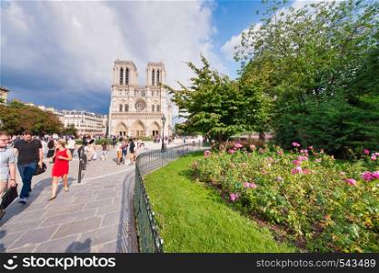 PARIS - JUNE 2014: Notre Dame Cathedral with tourists along the square garden. Notre Dame is visited by 12 million people every year.