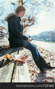 Park bench in autumn, woman sitting on it in the blurry background