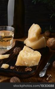 Parmigiano pieces on an old kitchen table, a glass of white wine and nuts. Lunch still life in Mediterranean style
