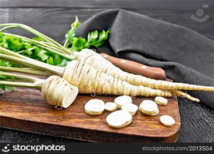 Parsley roots whole and chopped with green tops, knife, napkin on a black wooden board background
