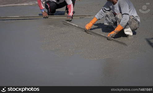Part of 2 construction workers using long triangle trowel to spread and plastering cement on the floor in construction site