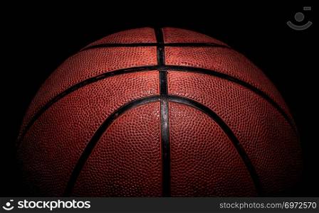 Part of basketball ball illuminated from above. On a black background.