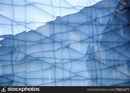 part of facade of geometrically shaped modern glass building with reflections of blue sky