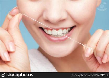 Part of female face. Young woman smiling girl cleaning her white teeth with dental floss on blue. Daily health care. Studio shot.