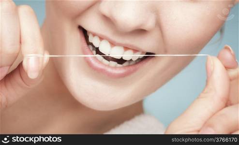Part of female face. Young woman smiling girl cleaning her white teeth with dental floss on blue. Daily health care. Studio shot.