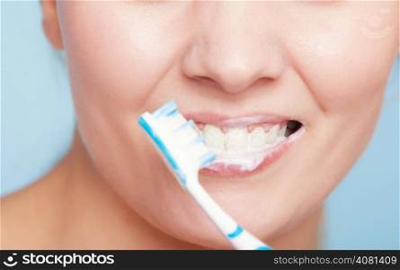 Part of female face. Young woman smiling girl with toothbrush brushing her white teeth on blue. Daily dental care. Studio shot.