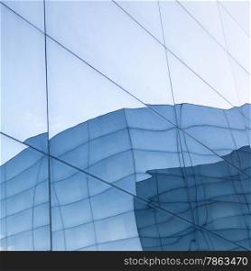 part of geometrically shaped modern glass building with reflections of blue sky and glass wall