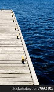 Part of gray wooden dock with metal cleats on blue water.