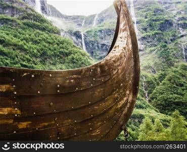 Part of old wooden viking boat in norwegian nature, mountains with waterfalls in the background. Tourism and traveling concept. Part of old wooden viking boat in norwegian nature