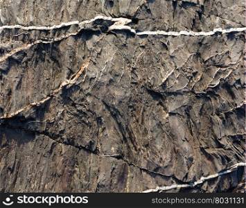Part of rock closeup with white stripes of another geological material. Nature background.
