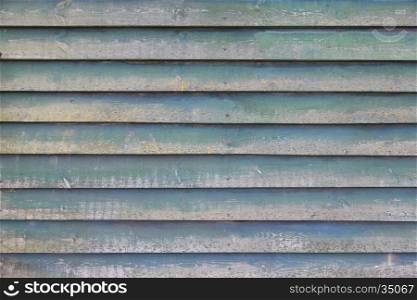 part of shed wall consisting of old horizontal wooden planks with faded green paint and yellow moss