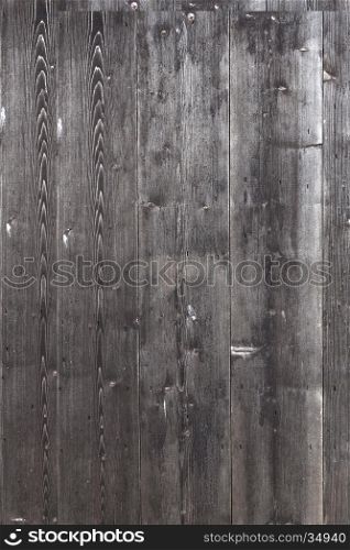 part of shed wall consisting of old vertical wooden planks with faded black or dark grey paint