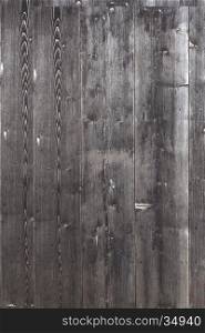 part of shed wall consisting of old vertical wooden planks with faded black or dark grey paint