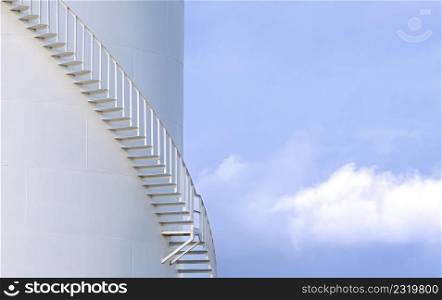 Part of spiral staircase on white fuel tank against cloud on blue sky background