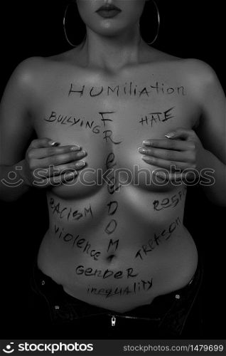 part of the body of a young girl with the inscription, humiliation, bullying, freedom, racism, violence . the captions are written in the photographer&rsquo;s hand, not in a tattoo . black and white photo.