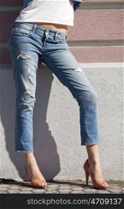 Part of the body, torn blue jeans for women on the background wall against the wall