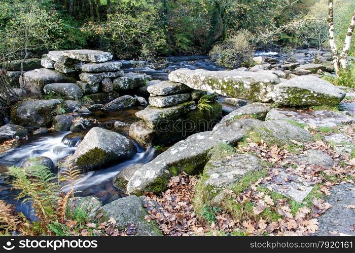 Partially collapsed ancient stone clapper bridge. Dartmeet, Dartmoor National Park, Devon, England, United Kingdom. Granite Bridge, autumn, fall, long exposure.