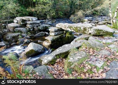 Partially collapsed ancient stone clapper bridge. Dartmeet, Dartmoor National Park, Devon, England, United Kingdom. Granite Bridge, autumn, fall, long exposure.