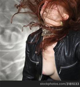 Partially nude Caucasian woman in leather jacket flipping long hair in air.