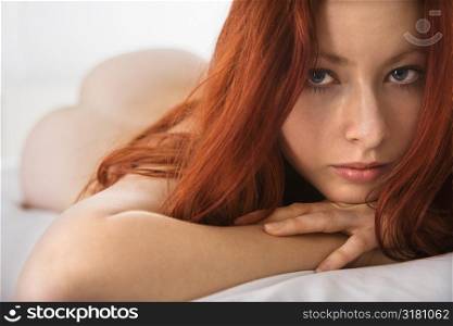Partially nude pretty young redhead woman lying on bed making eye contact.