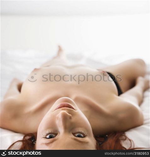 Partially nude topless pretty young redhead woman lying on bed.