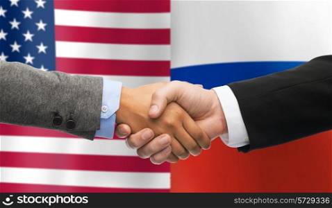 partnership, politics, gesture and people concept - close up of handshake over american and russian national flags background