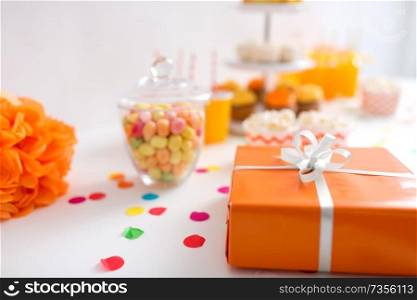 party and festive concept - close up of birthday present in orange wrap on table. birthday present in orange wrap on table at party