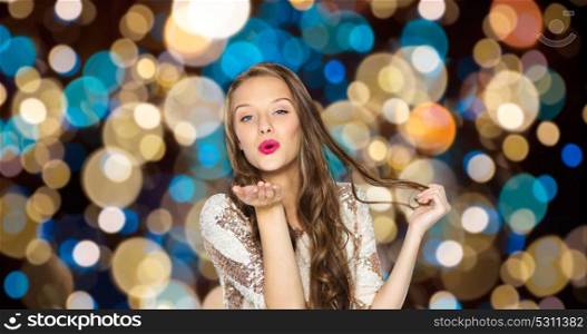 party and people concept - happy young woman in fancy dress with sequins and long wavy hair sending air kiss over festive lights background. happy woman sending air kiss over party lights