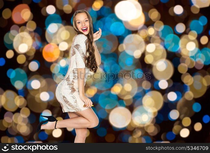 party and people concept - happy young woman or teen girl in fancy dress with sequins posing over festive lights background. happy young woman posing over party lights