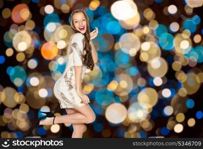 party and people concept - happy young woman or teen girl in fancy dress with sequins posing over festive lights background. happy young woman posing over party lights