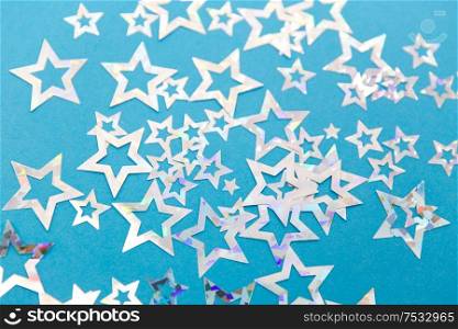 party, celebration and decoration concept - holographic star shaped confetti on blue background. star shaped confetti decoration on blue background