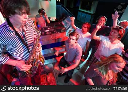 Party crowd going wild during a solo of a saxophonist, accompanied by a DJ